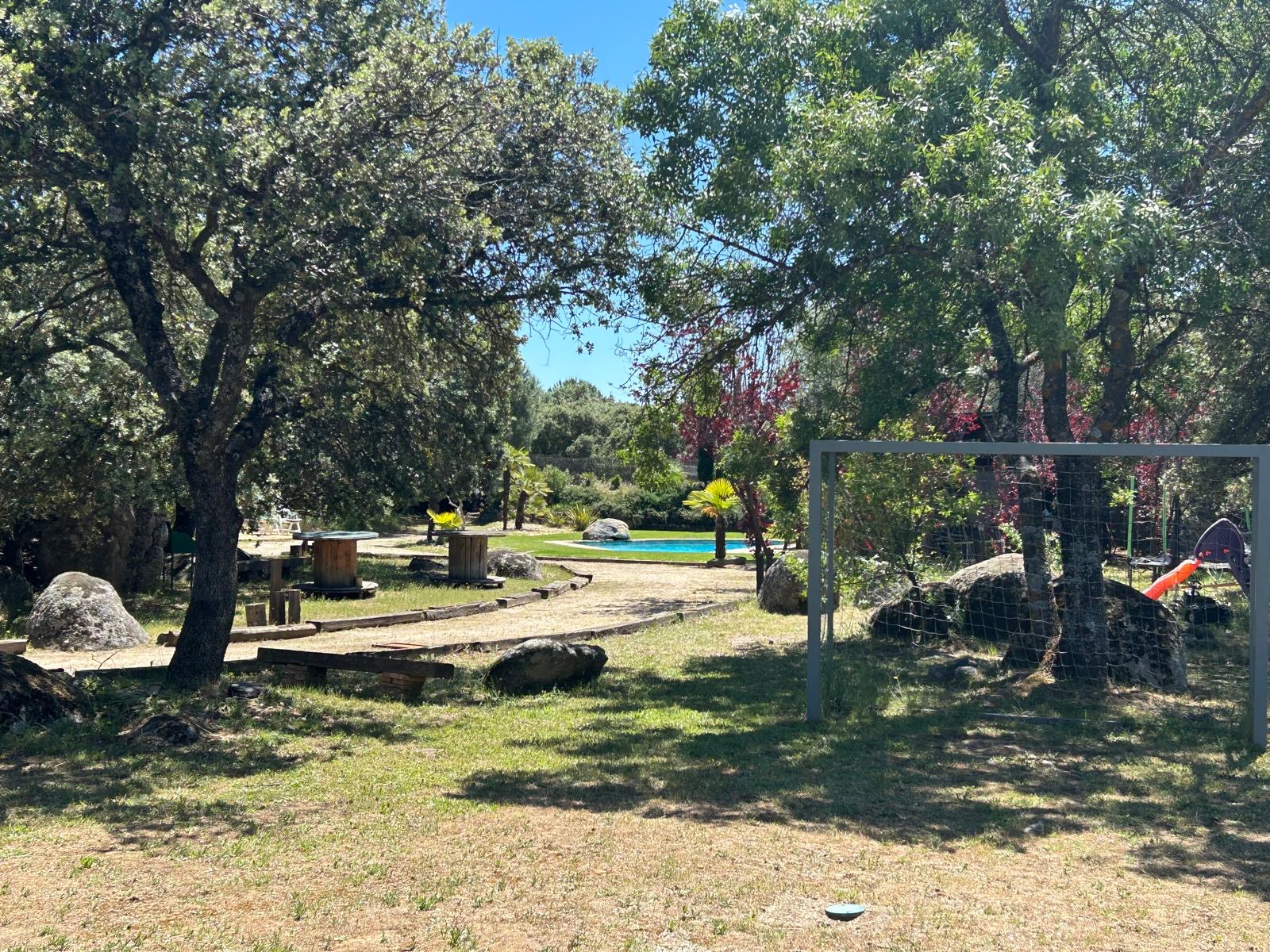 Zona de juegos entre árboles, con la piscina al fondo